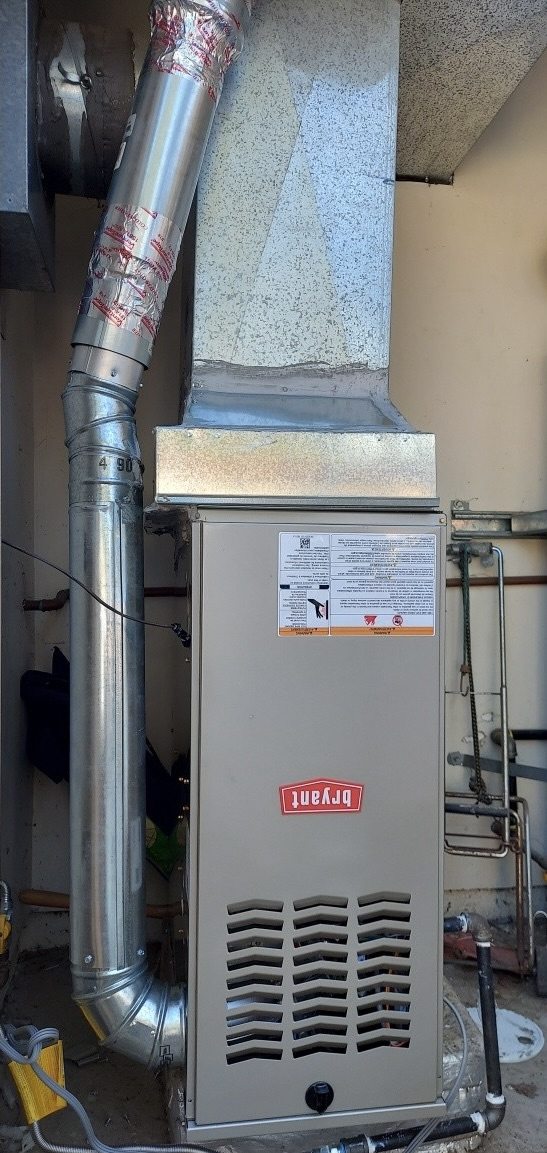 A new Bryant furnace in a utility space, with a metal flue and supply duct above it.