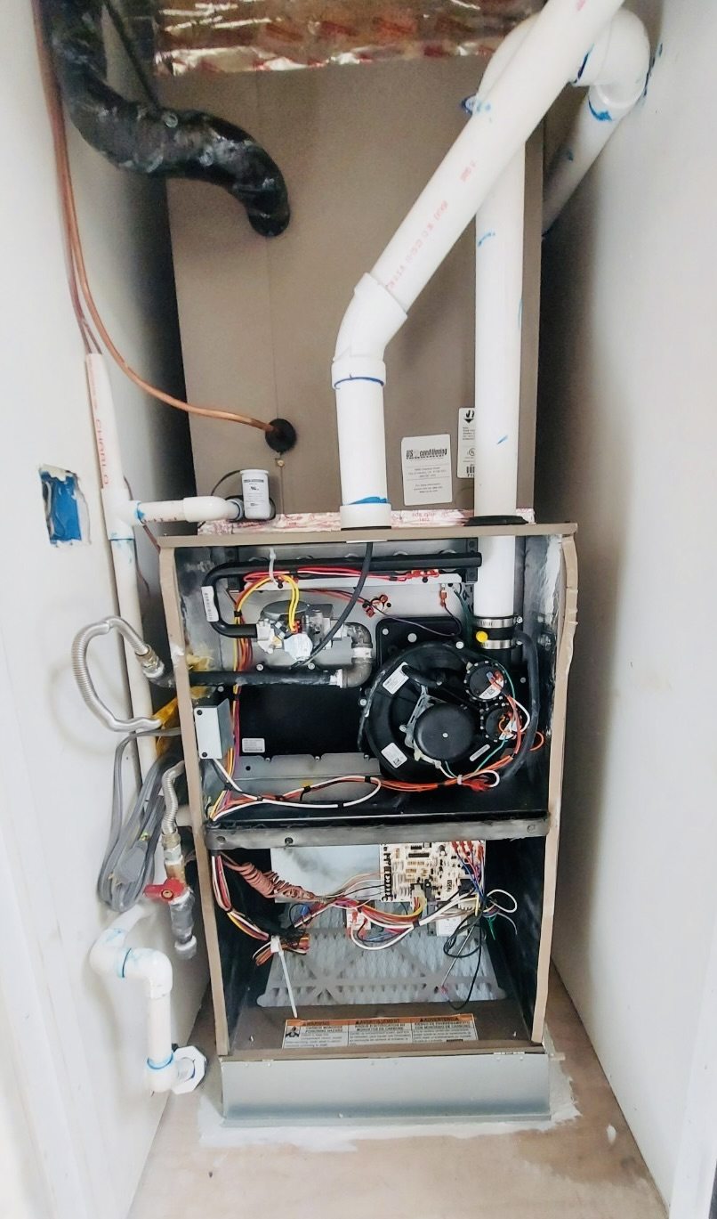 A furnace in a closet with its front panel off, showing the burner, blower and wiring, with white PVC venting above.